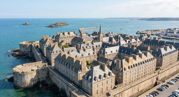 Vue a&eacute;rienne ou photographie de la c&ocirc;te et de la ville historique de Saint-Malo, montrant les remparts m&eacute;di&eacute;vaux, les toits de pierre et la mer en arri&egrave;re-plan, illustrant l'une des zones d'intervention principales de l'entreprise dans un rayon de 100 km.