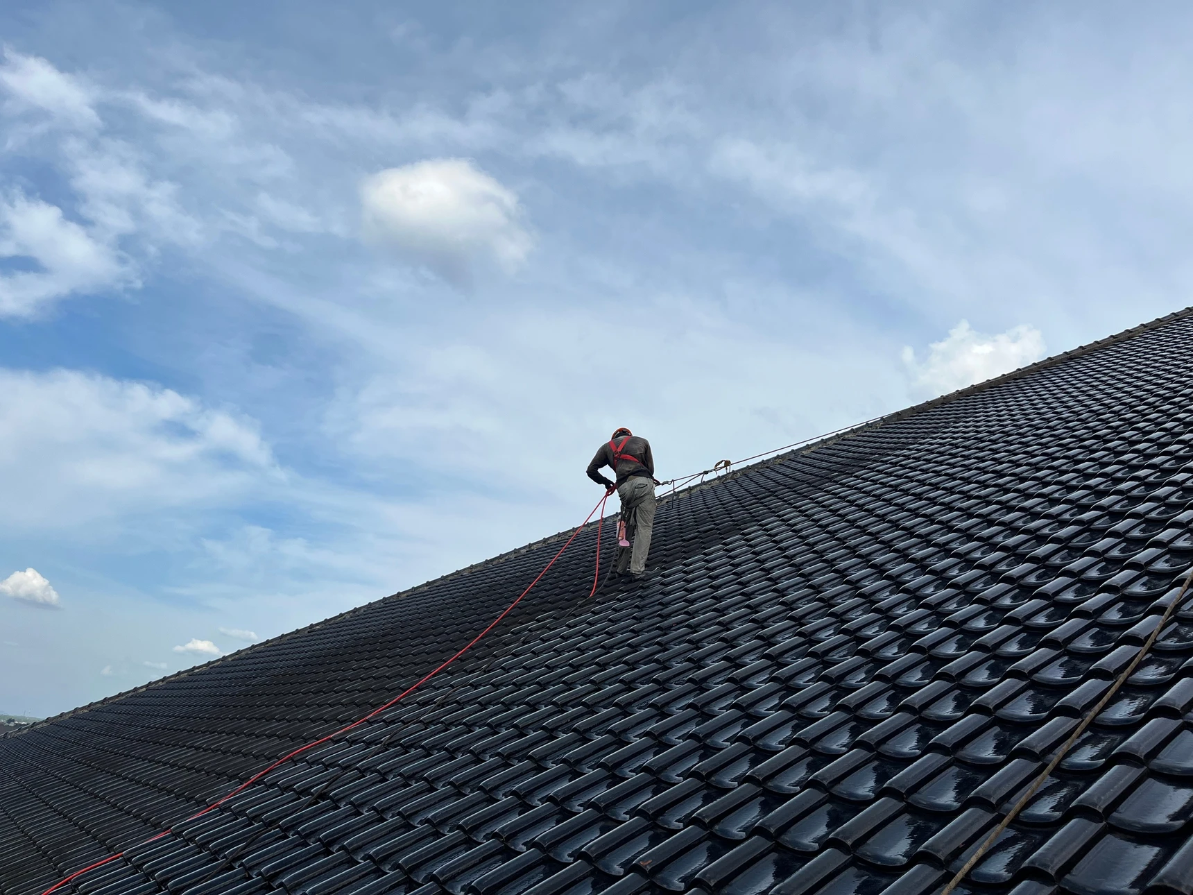 Scène extérieure sur toiture en tuiles rouges avec ouvrier effectuant un nettoyage haute pression d'une fenêtre de toit