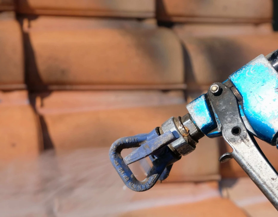 Ouvrier en combinaison de protection intégrale blanche travaillant sur toiture en ardoises, utilisant une échelle aluminium pour accéder aux tuiles défaillantes